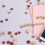 Moedas, calendário e celular com calculadora sobre uma mesa, ilustrando planejamento financeiro para pequenos negócios.