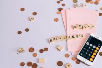 Moedas, calendário e celular com calculadora sobre uma mesa, ilustrando planejamento financeiro para pequenos negócios.