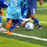 Crianças jogam futebol em um campo gramado, em uma cena de atividade esportiva coletiva.