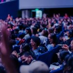 Público diversificado acompanha atentamente um evento em um auditório.