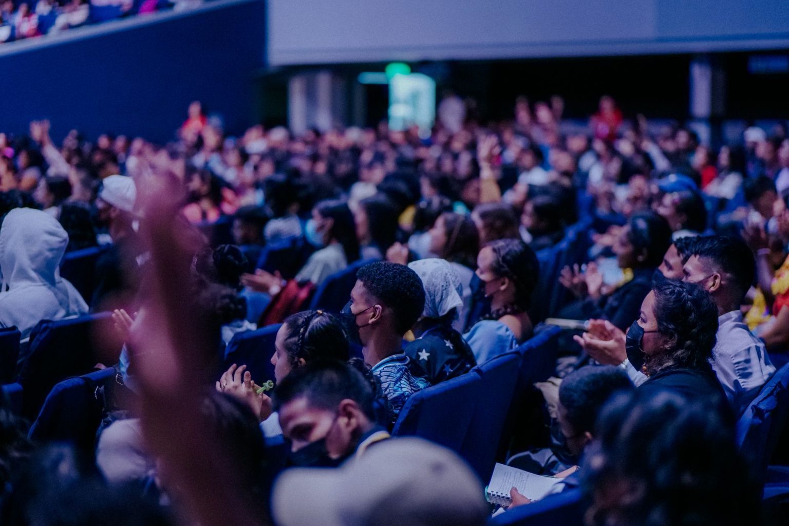 Público diversificado acompanha atentamente um evento em um auditório.