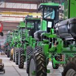 Máquinas agrícolas verdes enfileiradas dentro de um galpão industrial.