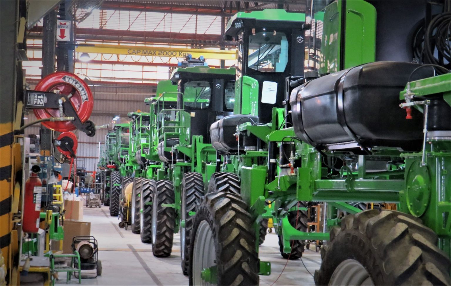 Máquinas agrícolas verdes enfileiradas dentro de um galpão industrial.