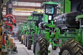 Máquinas agrícolas verdes enfileiradas dentro de um galpão industrial.