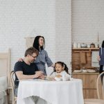 Família conversa à mesa com uma profissional da assistência social em ambiente doméstico.
