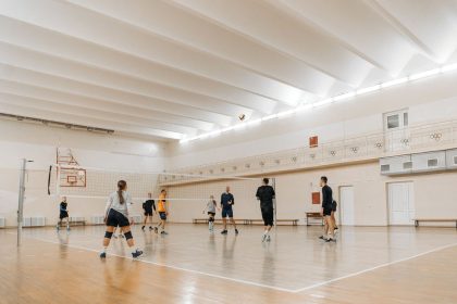 Atletas jogam vôlei em um ginásio esportivo coberto com piso de madeira.