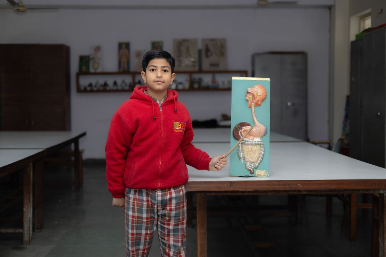 Estudante apresenta um modelo anatômico diante da turma em uma sala de aula.