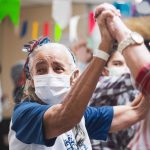 Grupo de idosos dança e comemora reunido em um ambiente interno.