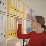 Mulher organiza e procura documentos em pastas coloridas em um escritório.
