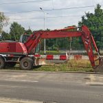 Escavadeira hidráulica vermelha ao lado de uma estrada em um canteiro de obras, durante o dia.