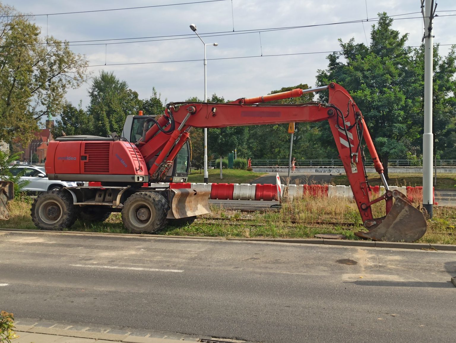 Escavadeira hidráulica vermelha ao lado de uma estrada em um canteiro de obras, durante o dia.