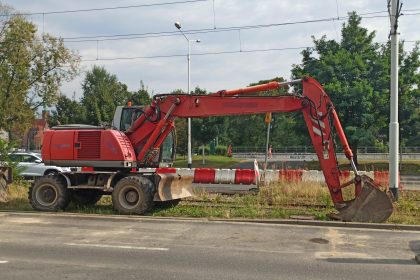 Escavadeira hidráulica vermelha ao lado de uma estrada em um canteiro de obras, durante o dia.